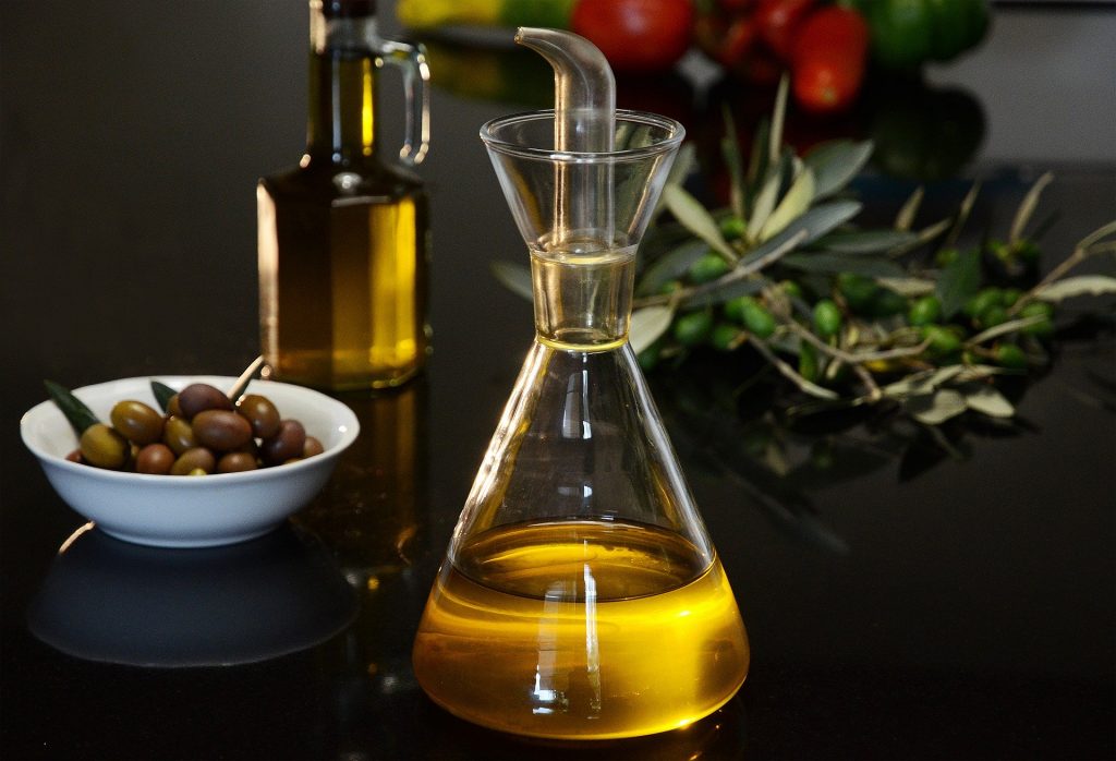 Deux bouteilles d'huile d'olive posée sur une table avec un bol rempli d'olives et une branche d'olivier