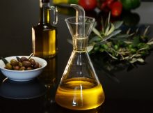 Deux bouteilles d'huile d'olive posée sur une table avec un bol rempli d'olives et une branche d'olivier