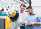 deux hommes regardant une tablette devant une machine industrielle