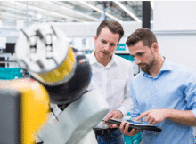 deux hommes regardant une tablette devant une machine industrielle